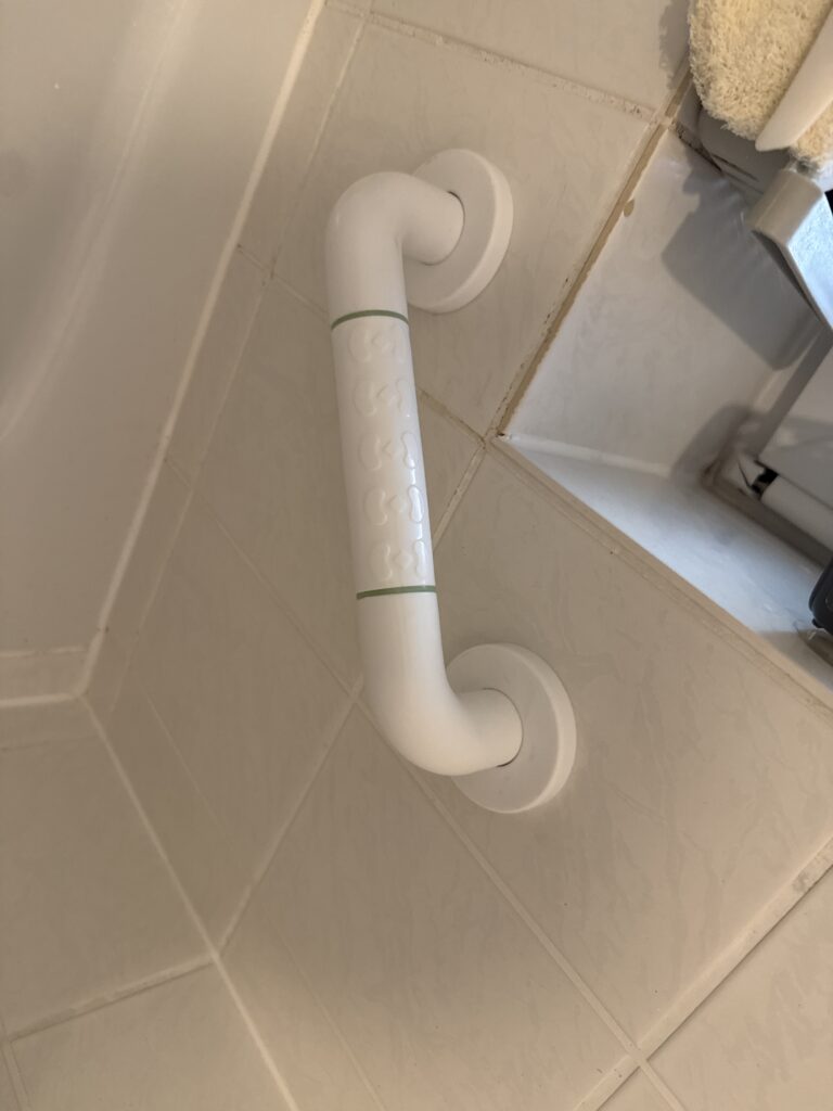 Ein weißer Haltegriff als Einstiegshilfe Badewanne an einer gefliesten Wand, ideal für eine seniorengerechte Badlösung und barrierefreie Badewanne. - Wannentüren.de